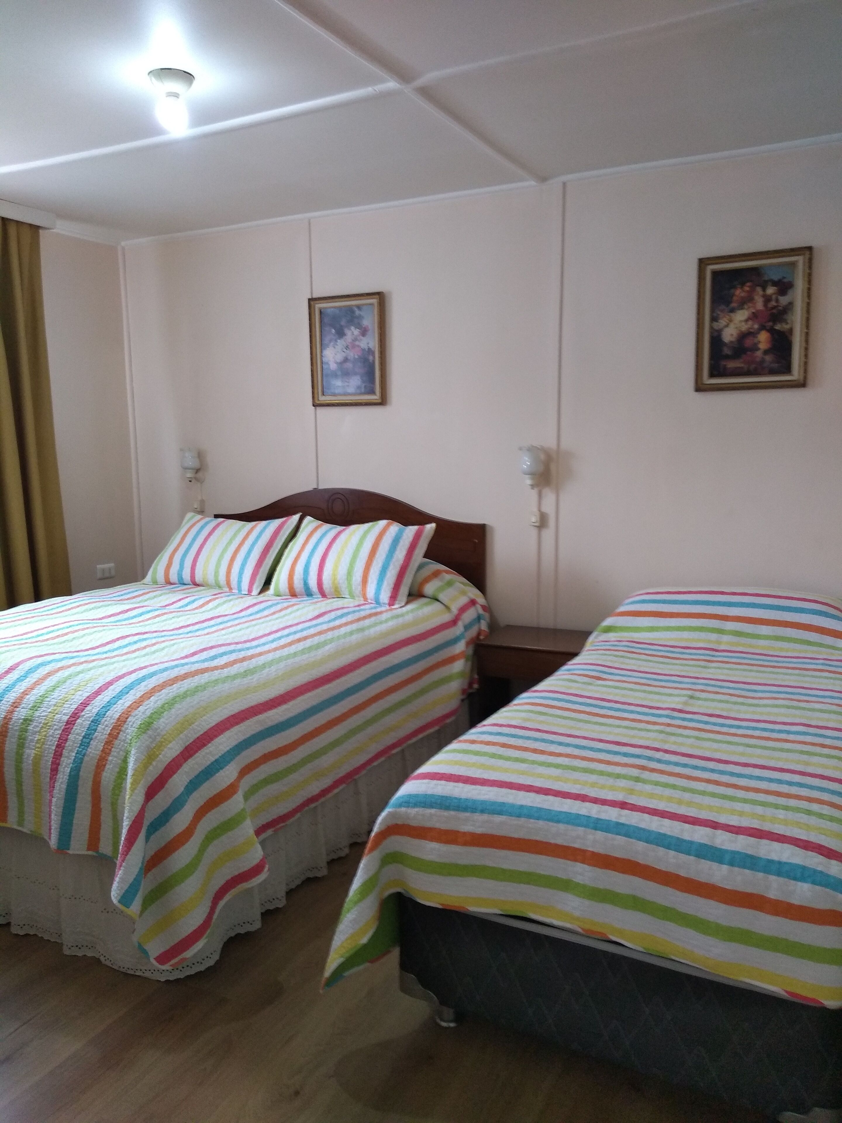 Una habitación con dos camas, cada una con ropa de cama a rayas, cabeceros de madera y una mesita de noche. Hay dos cuadros enmarcados en la pared.