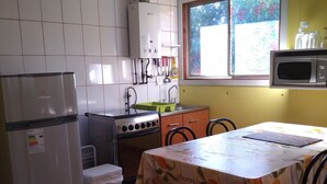 Una cocina compacta con armarios blancos, estufa, microondas y un ventanal con estampado floral.