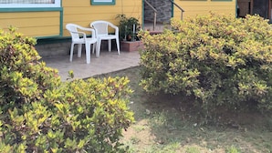 Un edificio amarillo con un porche, dos sillas blancas y un muro de piedra.