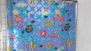 A bathroom with a colorful shower curtain featuring marine life, a white toilet, and a blue rug. - Sapphire House (Caye Caulker)
