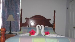 A bed with a wooden headboard, floral pillows, and a bedspread with a two swan design. - Sapphire House (Caye Caulker)