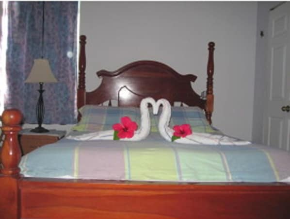 A bed with a wooden headboard, floral pillows, and a bedspread with a two swan design. - Sapphire House (Caye Caulker)