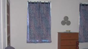 A room with a blue sofa, a wooden dresser, and a window with patterned curtains. - Sapphire House (Caye Caulker)