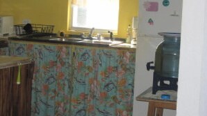 A kitchen with a sink, a refrigerator, and a window with curtains. - Sapphire House (Caye Caulker)
