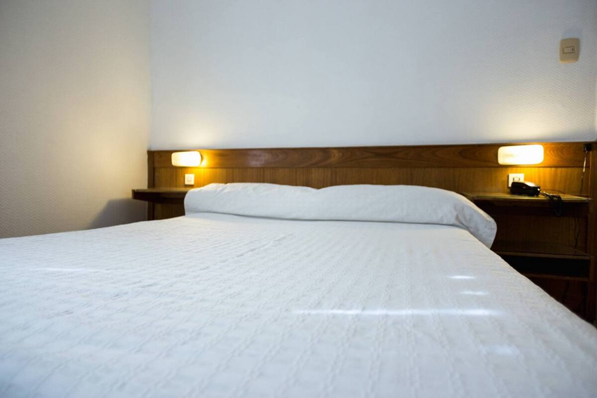 A neatly made bed with a wooden headboard, two bedside lamps, and a nightstand with a telephone.
