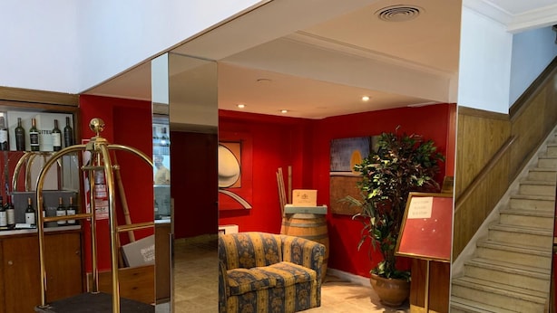 A room with a red wall, a wooden staircase, a small seating area, and a cart with wine bottles. - Palace Hotel Mendoza (Mendoza)
