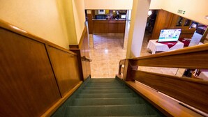 A wooden staircase with a carpeted landing and a view of a reception area with a laptop on a table. - Palace Hotel Mendoza (Mendoza)