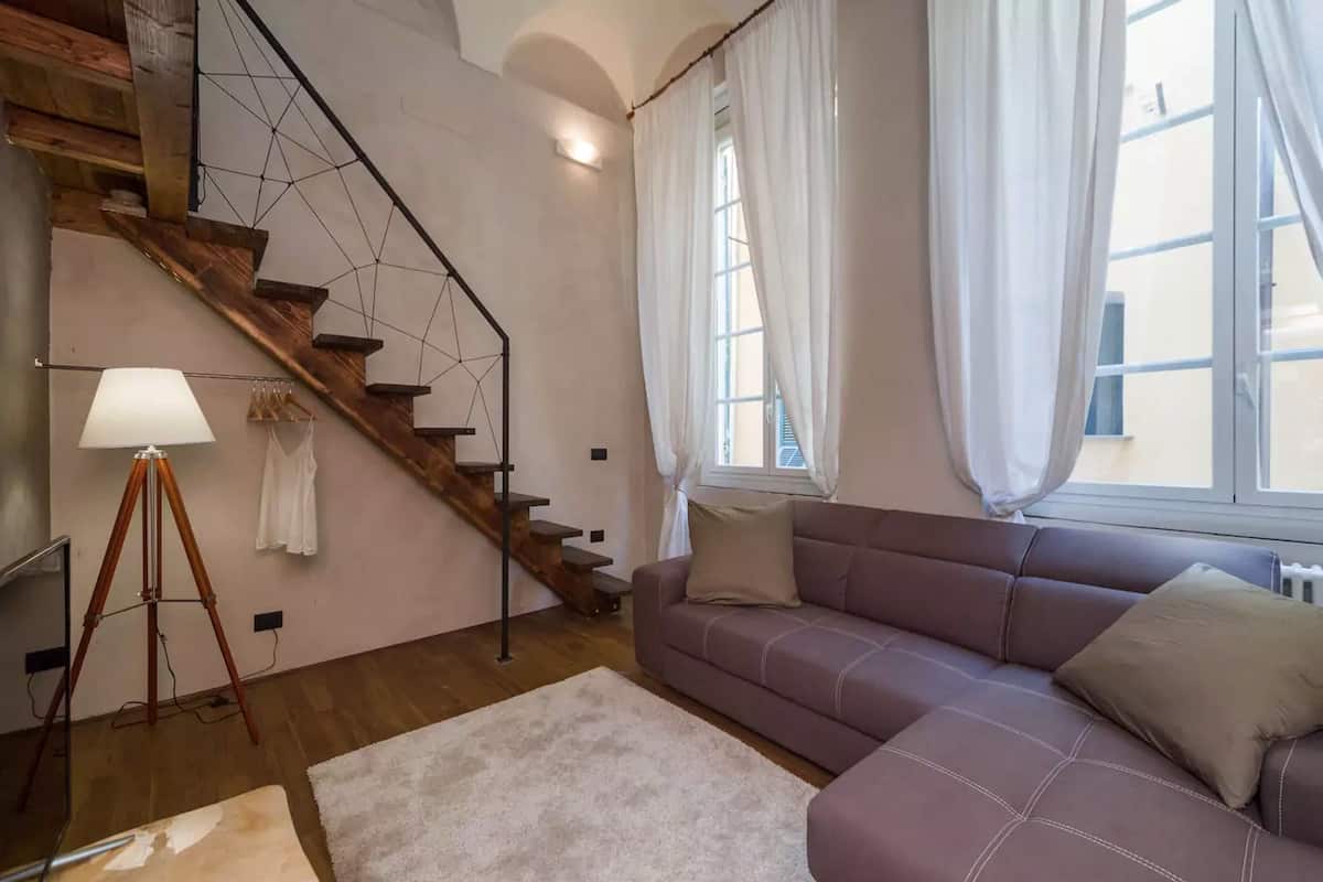 A living room with a wooden staircase, a sofa, a lamp, and a window with curtains.