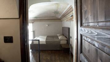 A narrow doorway leading to a bedroom with a bed, a bench, and a ceiling with decorative moldings.