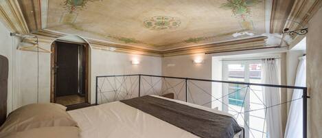 A bedroom with a bed, a wooden floor, a decorative ceiling, and a window with curtains.