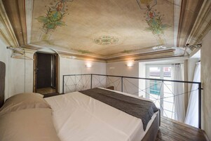 Een slaapkamer met een bed, een houten vloer, een decoratief plafond en een raam met gordijnen.