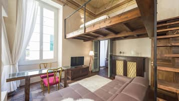 A loft-style room with a high ceiling, exposed wooden beams, a glass dining table, a sofa, and a fireplace.