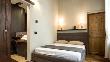 Una camera da letto con un letto grande, una porta in legno, un piccolo ripiano con dei libri e un bagno con lavandino e specchio.