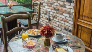 A dining area with a glass table, wooden chairs, and a brick wall with decorative panels. - Pousada Rosa Gramado (Gramado)