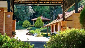 A covered entrance with a brick wall, a sign indicating a house of alarm, and a garden with a gazebo. - Pousada Rosa Gramado (Gramado)