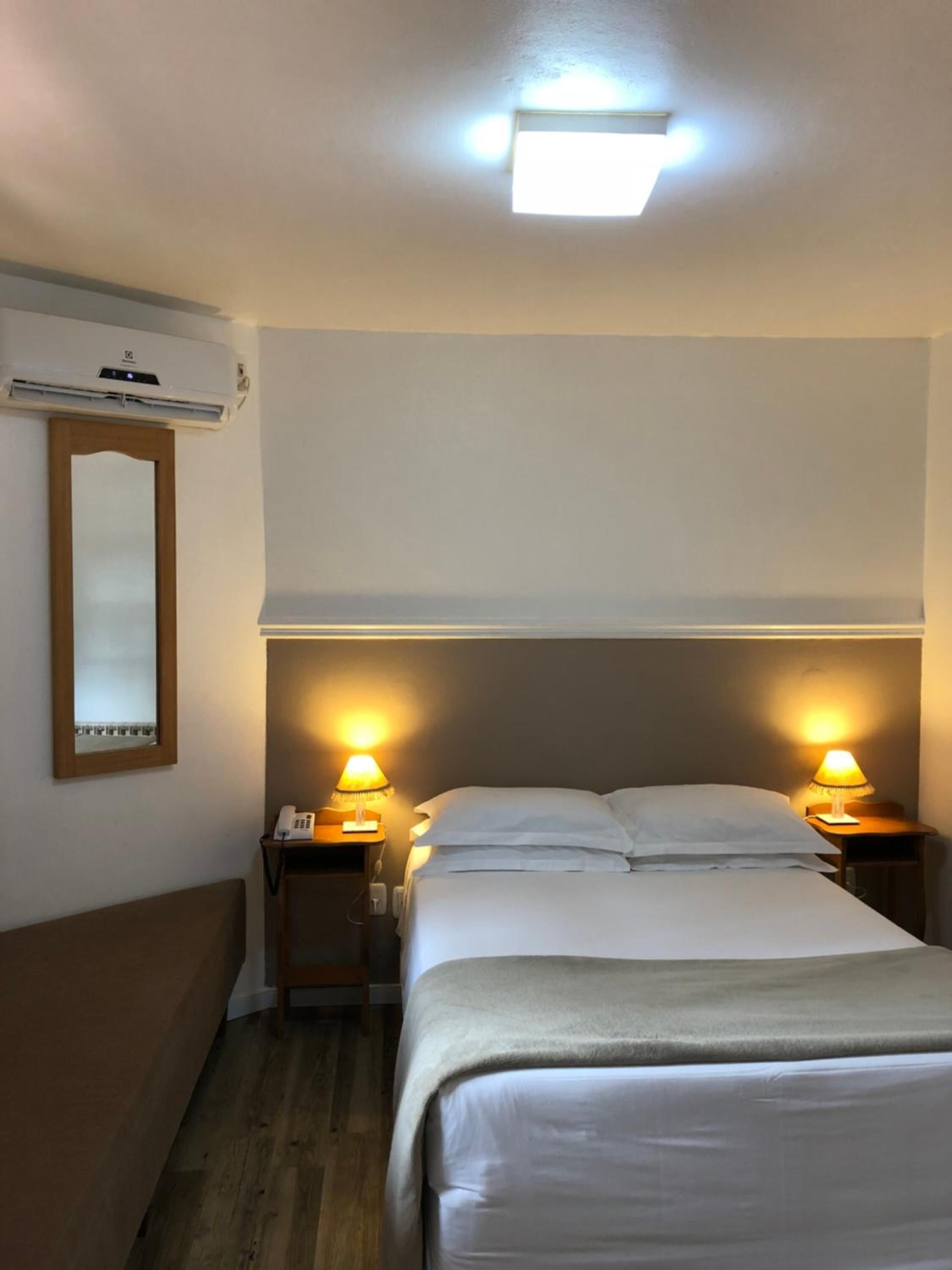 Une chambre d’hôtel équipée d’un lit, de deux lampes de chevet, d’un téléphone, d’un appareil de climatisation et d’un miroir mural.