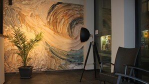 Un vestíbulo con un gran mural abstracto, una planta en maceta, un trípode con un sombrero y una silla de mimbre.