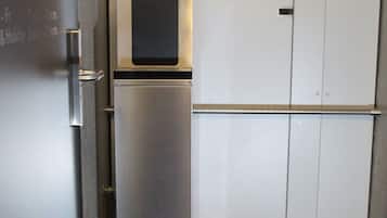 Un refrigerador compacto con dispensador de agua y compartimento congelador, ubicado contra una pared con una puerta y un mueble pequeño.