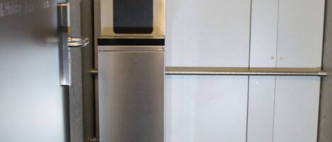 Un refrigerador compacto con dispensador de agua y compartimento congelador, ubicado contra una pared con una puerta y un mueble pequeño.