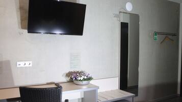 Una habitación con una televisión de pantalla plana montada en la pared, una mesita con un cuenco de flores, una silla y un banco.