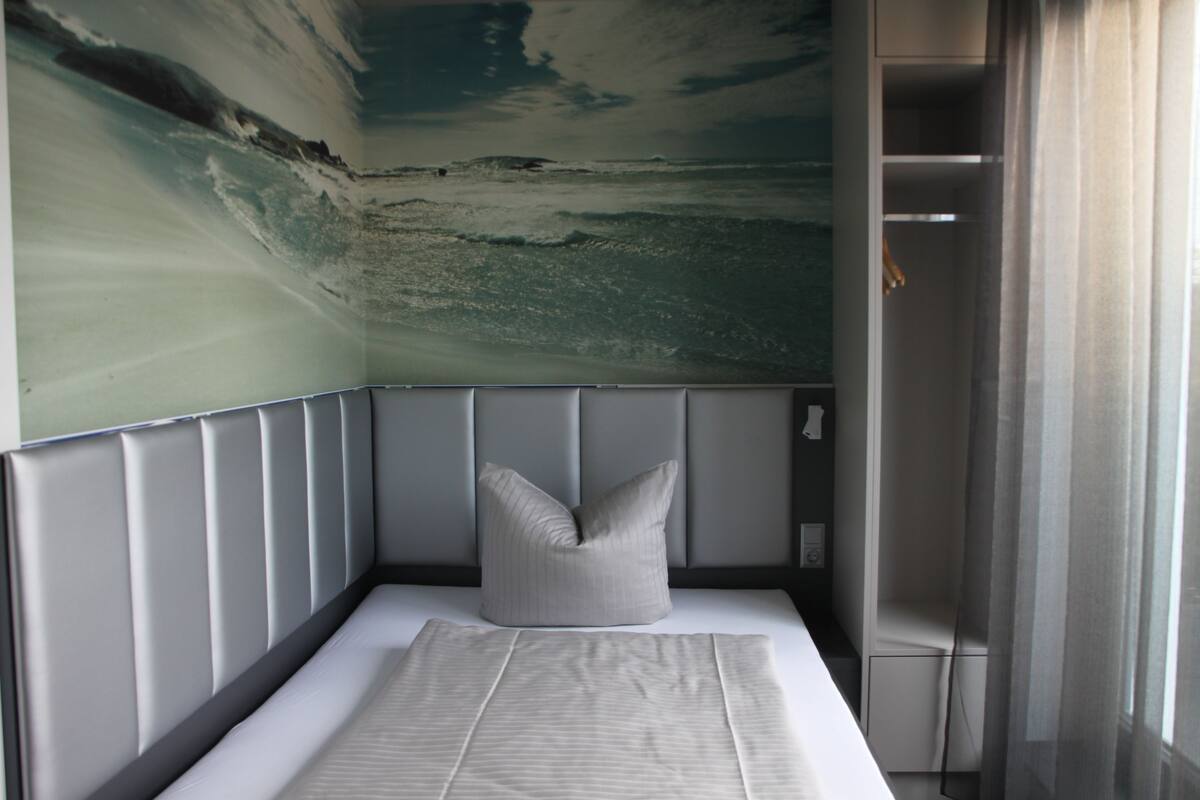 A bedroom with a bed, a pillow, a headboard, and a wall mural of a beach scene.