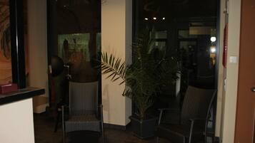 A lobby with wicker chairs, a potted plant, and a glass door leading to another area.