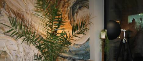 Una habitación con un cuadro abstracto grande, una planta en maceta y un trípode con una cámara.