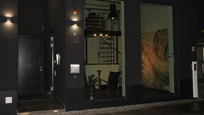 Una entrada moderna de edificio con un gran ventanal, una escalera y un pequeño espacio de descanso con una mesa y sillas.