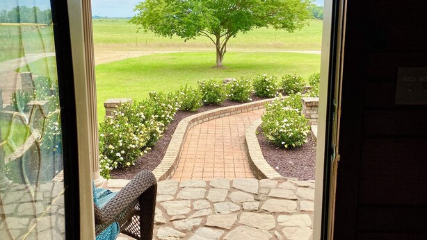 A view from a vehicle's open door to a landscaped area with a paved path, a bench, and a tree. - Southern Backroad Retreats (The Pool House) (Goshen)