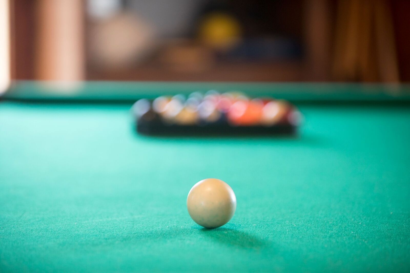 Una mesa de billar con una única bola blanca en foco y un juego de bolas de colores al fondo.