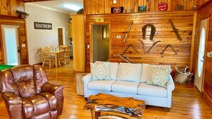 A cozy room with a leather armchair, a light blue sofa, and a rustic wooden coffee table. - Southern Backroad Retreats (The Pool House) (Goshen)