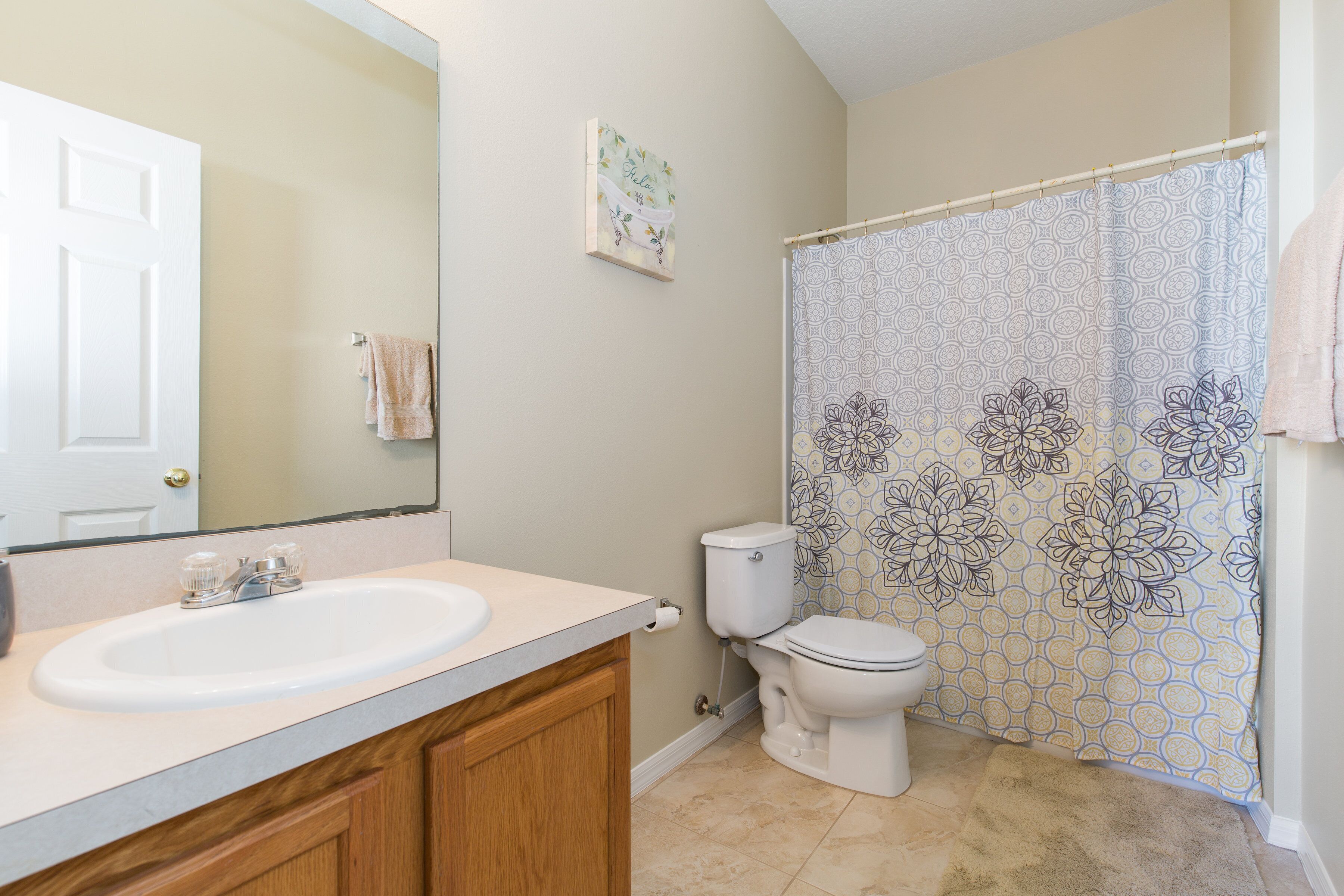 Une salle de bain avec un lavabo blanc, des meubles en bois, des toilettes et un rideau de douche à motifs floraux.