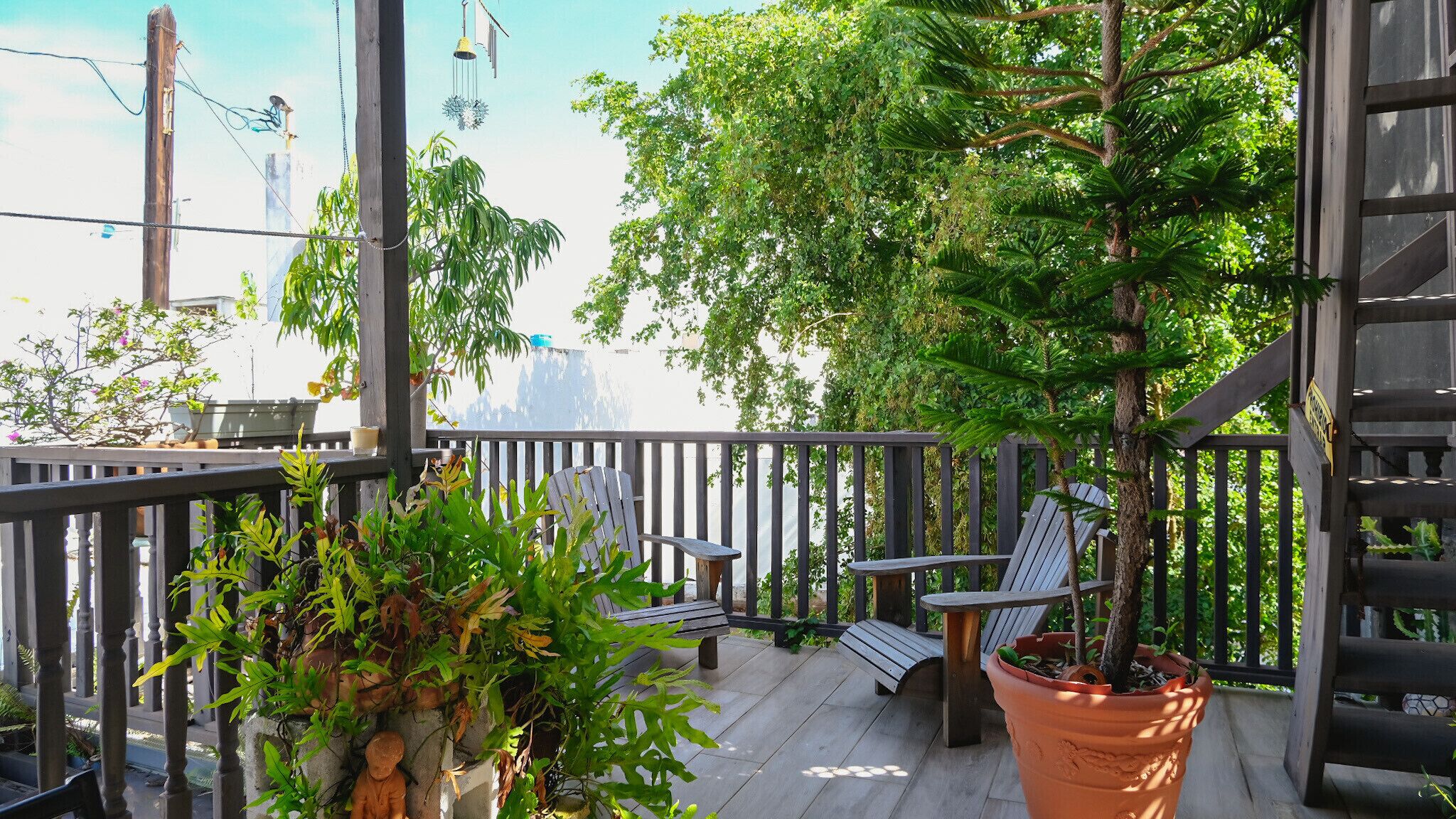 Een houten terras met een bankje en een tafel, omringd door potplanten en uitzicht op een waterpartij.