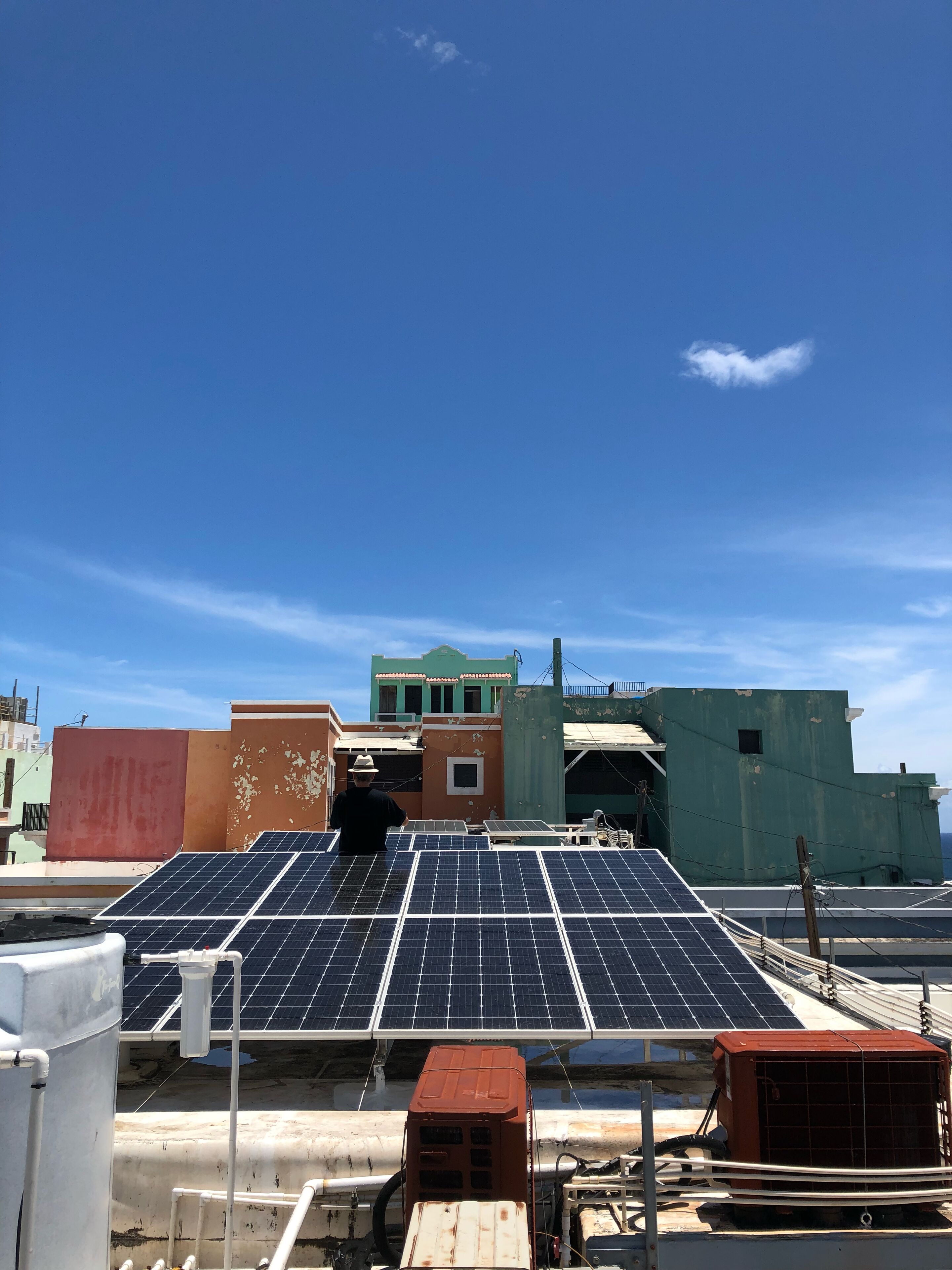 A rooftop with solar panels, a green building in the background, and a person standing.