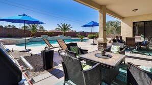 A patio with outdoor furniture, a pool, and two blue umbrellas.