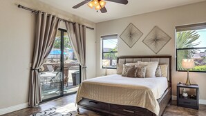 A bedroom with a bed, a ceiling fan, a nightstand, and a view of the outdoors.
