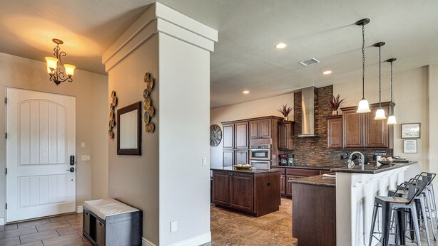 A spacious kitchen with a central island, pendant lighting, and a view into the living area.