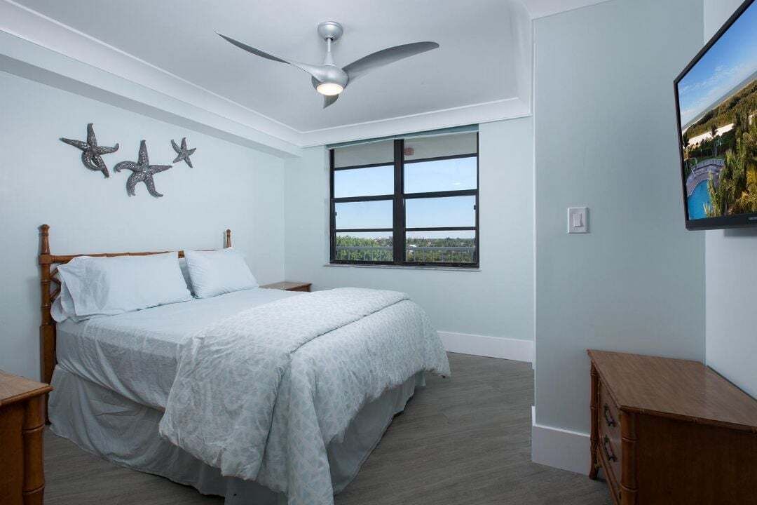 Un dormitorio con una cama, ventilador de techo, ventana y televisor.