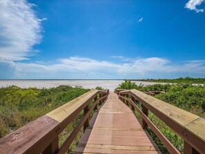 A wooden boardwalk leading to a beach with a clear sky.