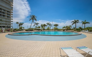 A swimming pool with a hexagonal tiled deck, surrounded by lounge chairs and palm trees.