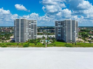 Two high-rise buildings with a swimming pool and greenery in the foreground.