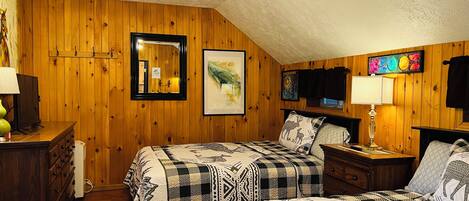 Een kamer met houten wanden, een plafondventilator, een bed met beddengoed met patroon, een dressoir, een nachtkastje en een ingelijst beeld aan de muur.