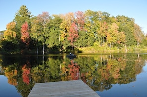 A calm lake with a wooden dock extending into the water, surrounded by trees with autumn foliage.