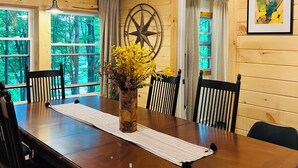 Un interior de madera con una mesa de comedor, sillas, una araña y una brújula estelar, además de un cuadro enmarcado.