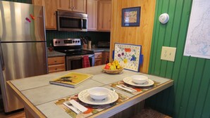 Cocina con armarios de madera, electrodomésticos de acero inoxidable, microondas y estufa. Hay un frutero, un cuadro enmarcado y un mapa en la pared.