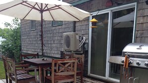 Un patio al aire libre con un deck de madera, una mesa con sillas, un gran paraguas, una parrilla y una planta en maceta.