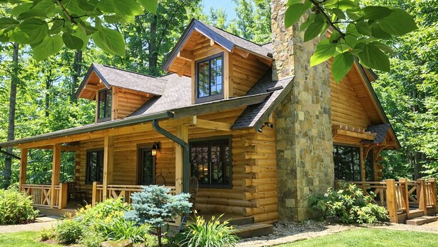 A log cabin with a porch, stone foundation, and a garden.