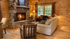 A cozy cabin interior with a stone fireplace, a sofa, a chair, and a dining table.