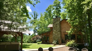 A rustic cabin with a stone chimney, surrounded by a well-maintained lawn and trees.
