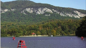 A lake with a rocky mountain in the background, a red lifeguard chair, and a small pavilion.